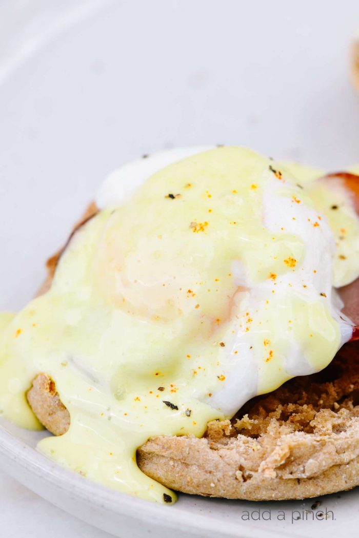 Toasted English muffins topped with Canadian bacon and poached eggs and drizzled with hollandaise sauce, all on a white plate.