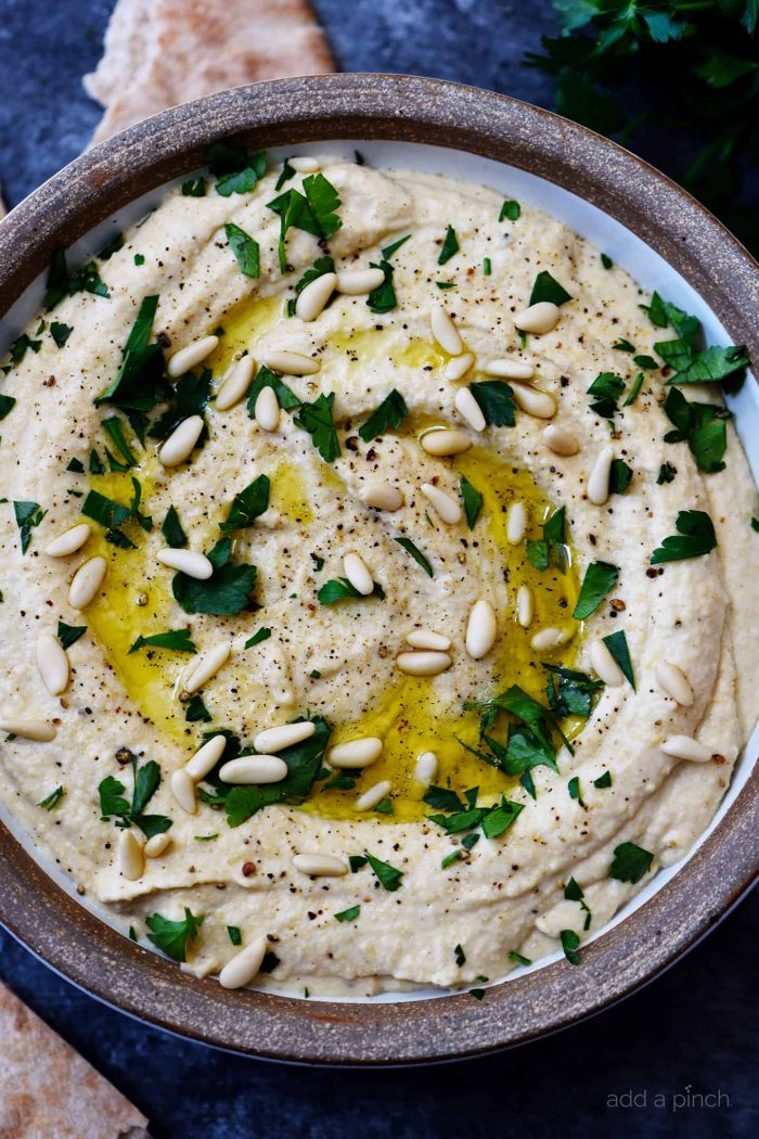 Hummus topped with olive oil and pine nuts and chopped fresh parsley in a stone serving bowlย // addapinch.com