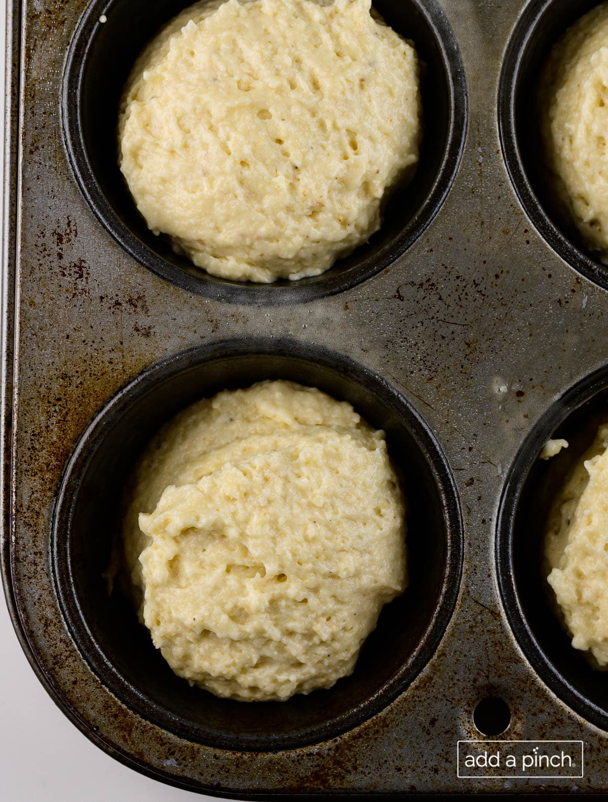 Photograph of cornbread muffin batter distributed in a muffin pan.