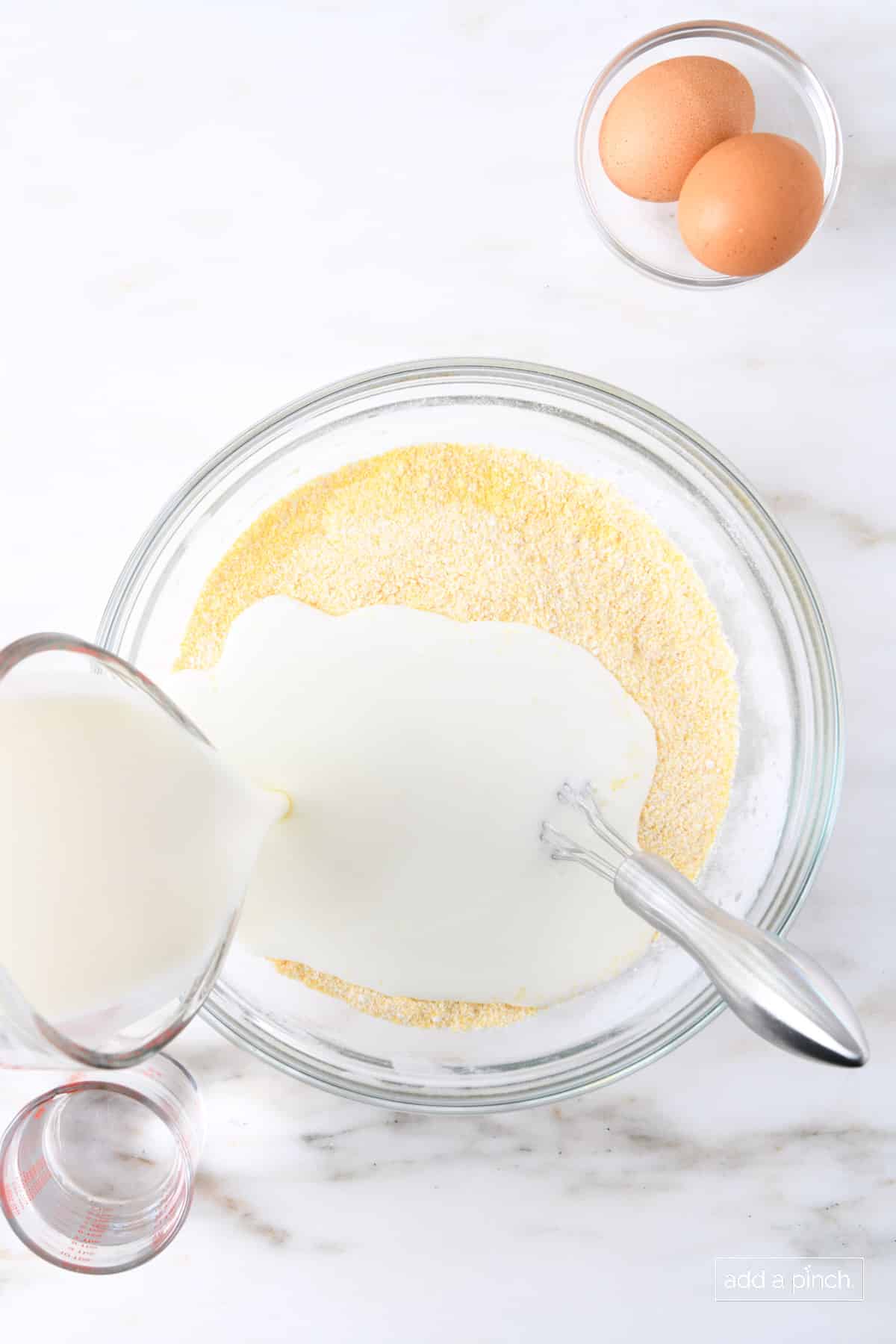 Pouring buttermilk into cornmeal mixture in a glass bowl.
