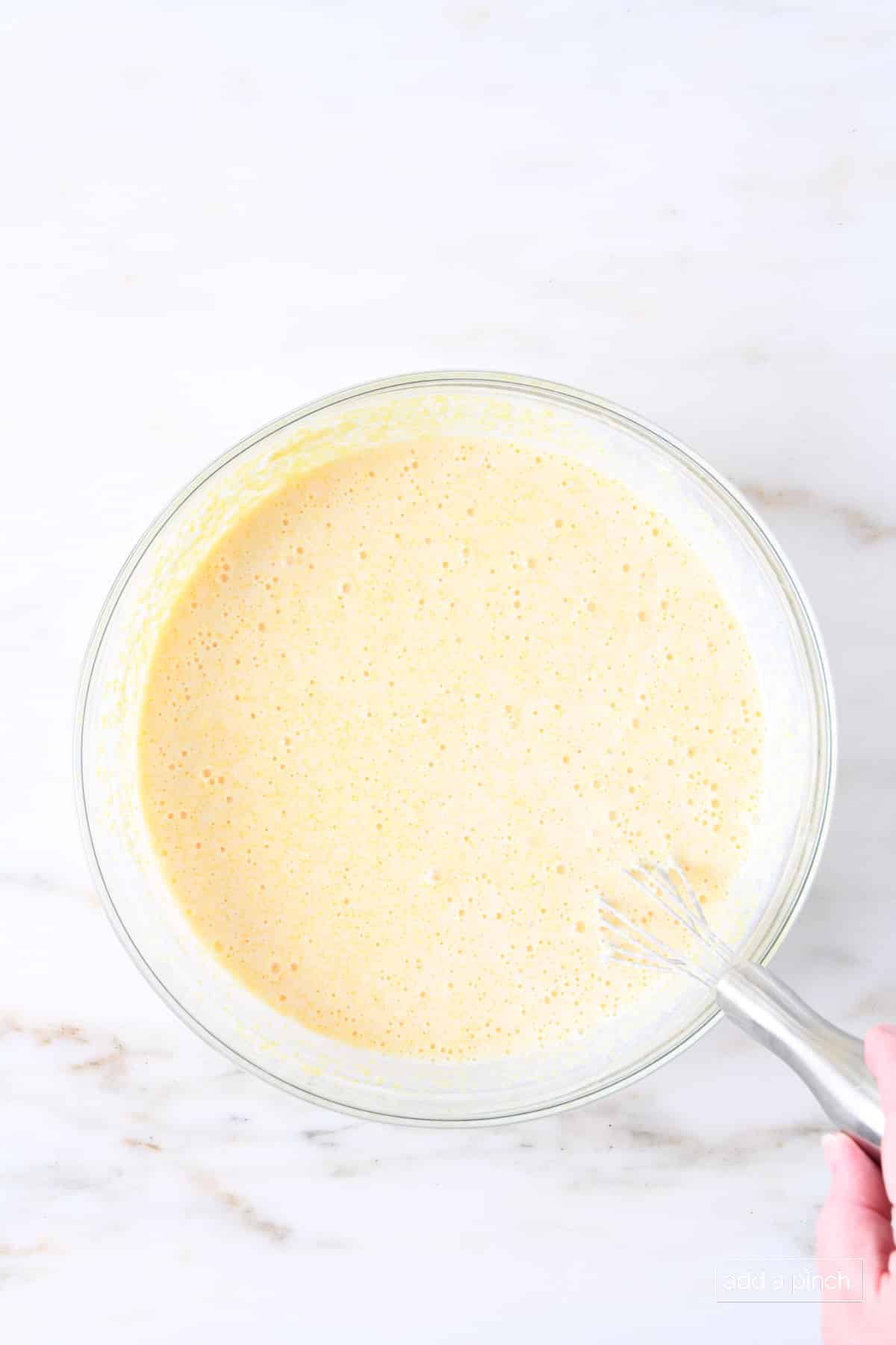 Whisked together homemade cornbread batter in a glass bowl with a metal whisk.