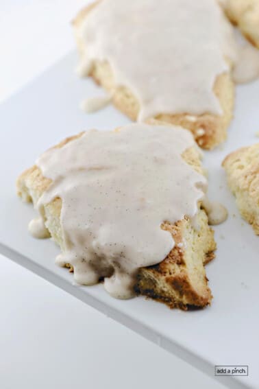 Scones topped with a vanilla bean glaze on a white platter.