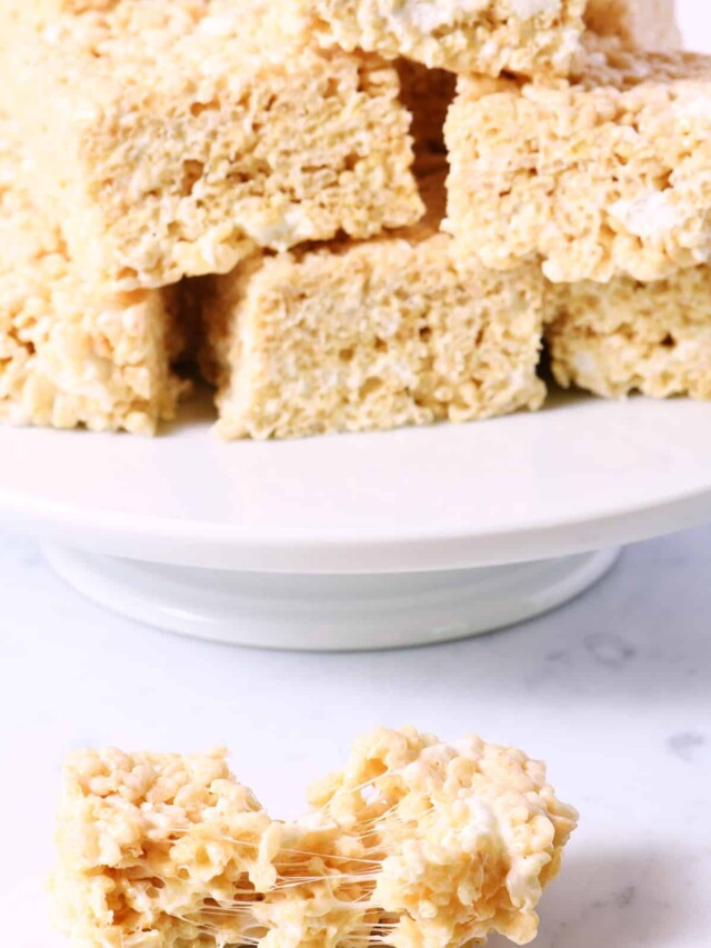 Rice cereal treats on a white bake plate with one in front.
