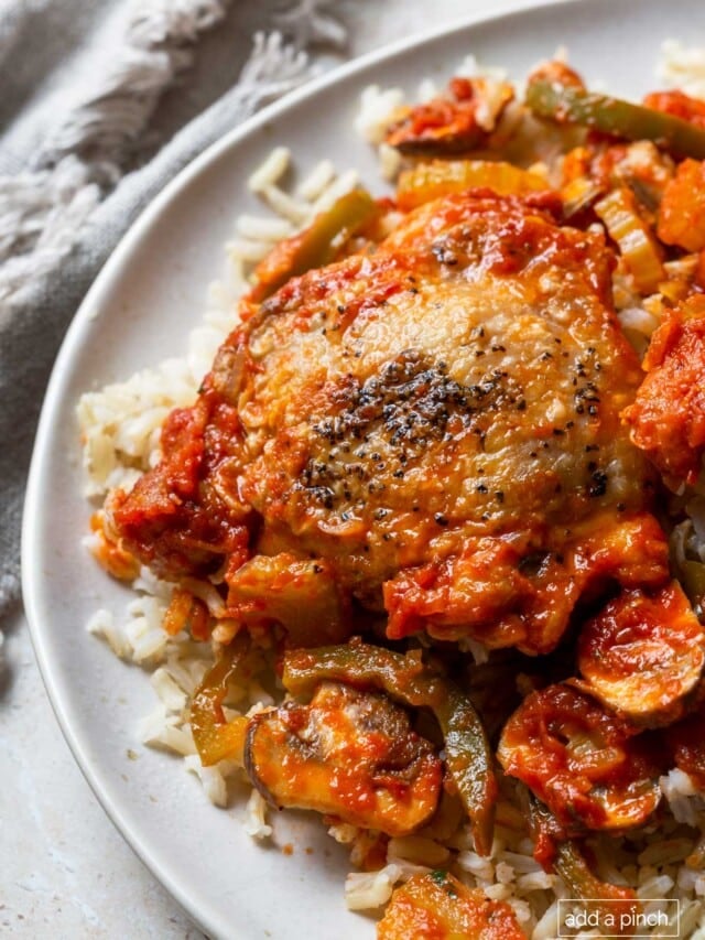 Photo of chicken cacciatore with chicken, peppers, and mushrooms on rice on a white plate.