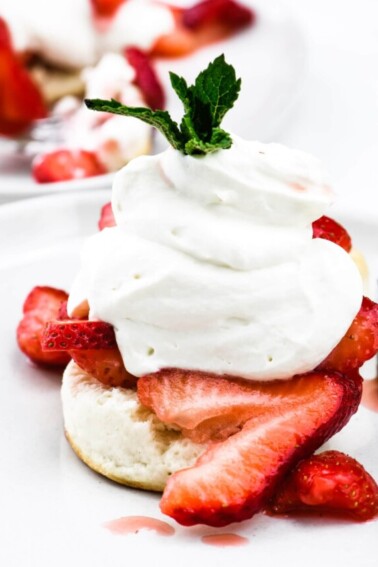 Strawberry shortcake topped with homemade whipped cream and mint sprig on a white plate. // addapinch.com
