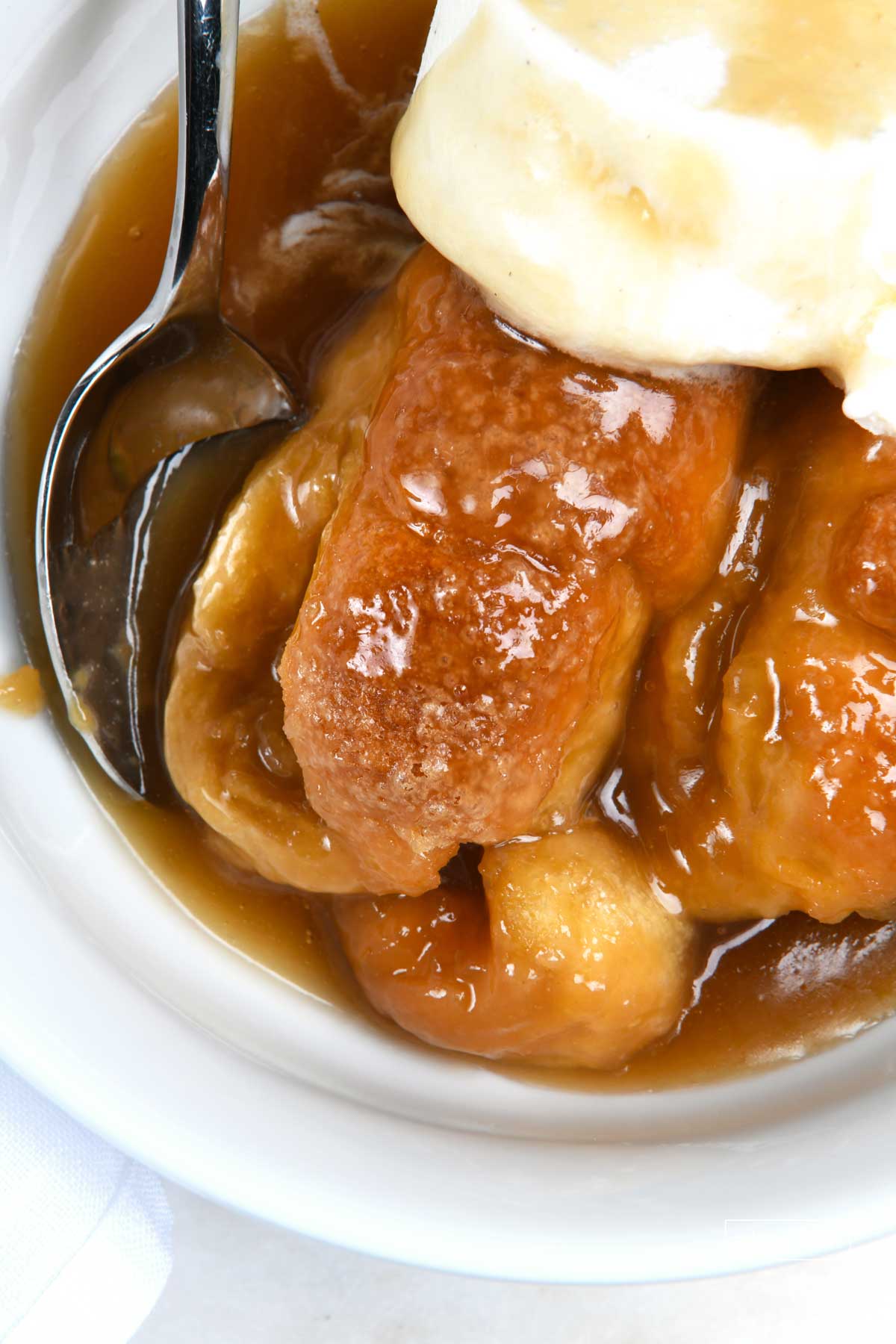 Photo of easy apple dumpling recipe in a white bowl topped with vanilla ice cream.