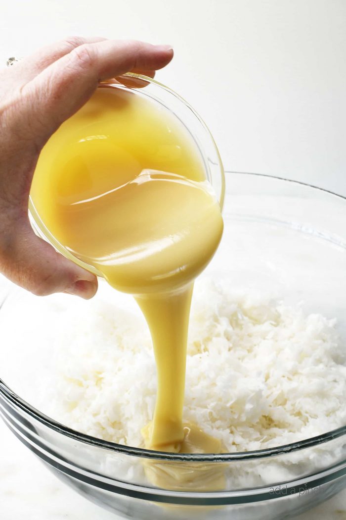 Glass bowl of coconut flakes with sweetened condensed milk being poured over it.