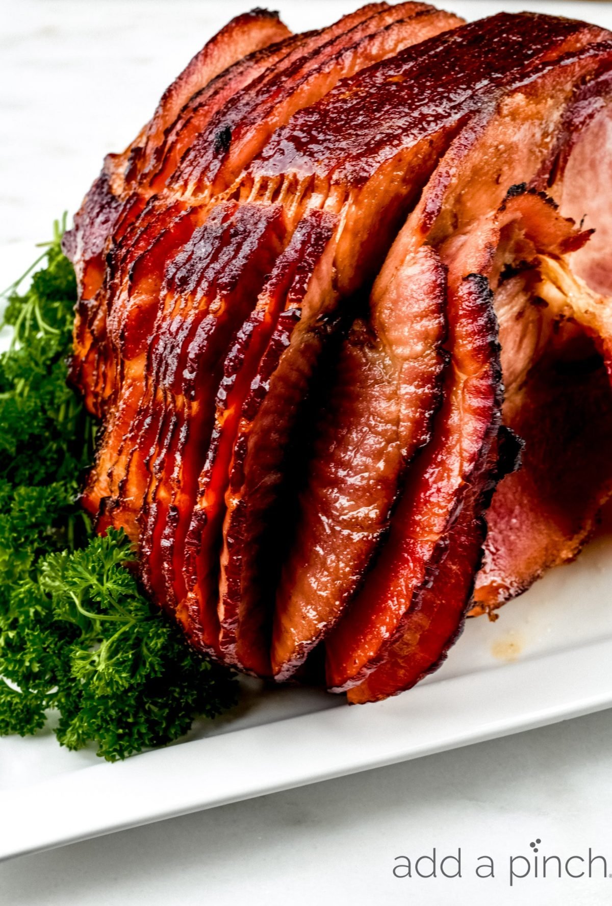 Photo of baked ham spiral sliced with gree parsley on white plate.