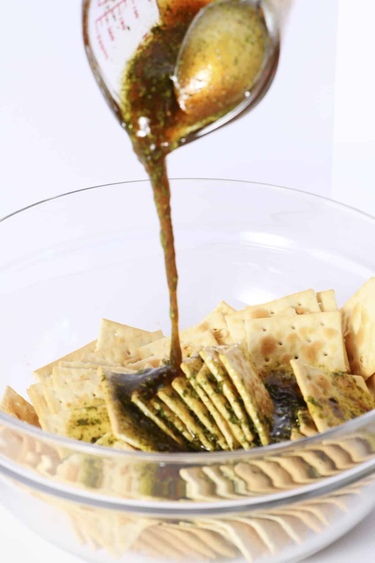 Pouring spicy marinade over saltine crackers in a glass mixing bowl.