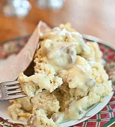 Photograph of giblet gravy on top of cornbread dressing with turkey on a holiday plate. 