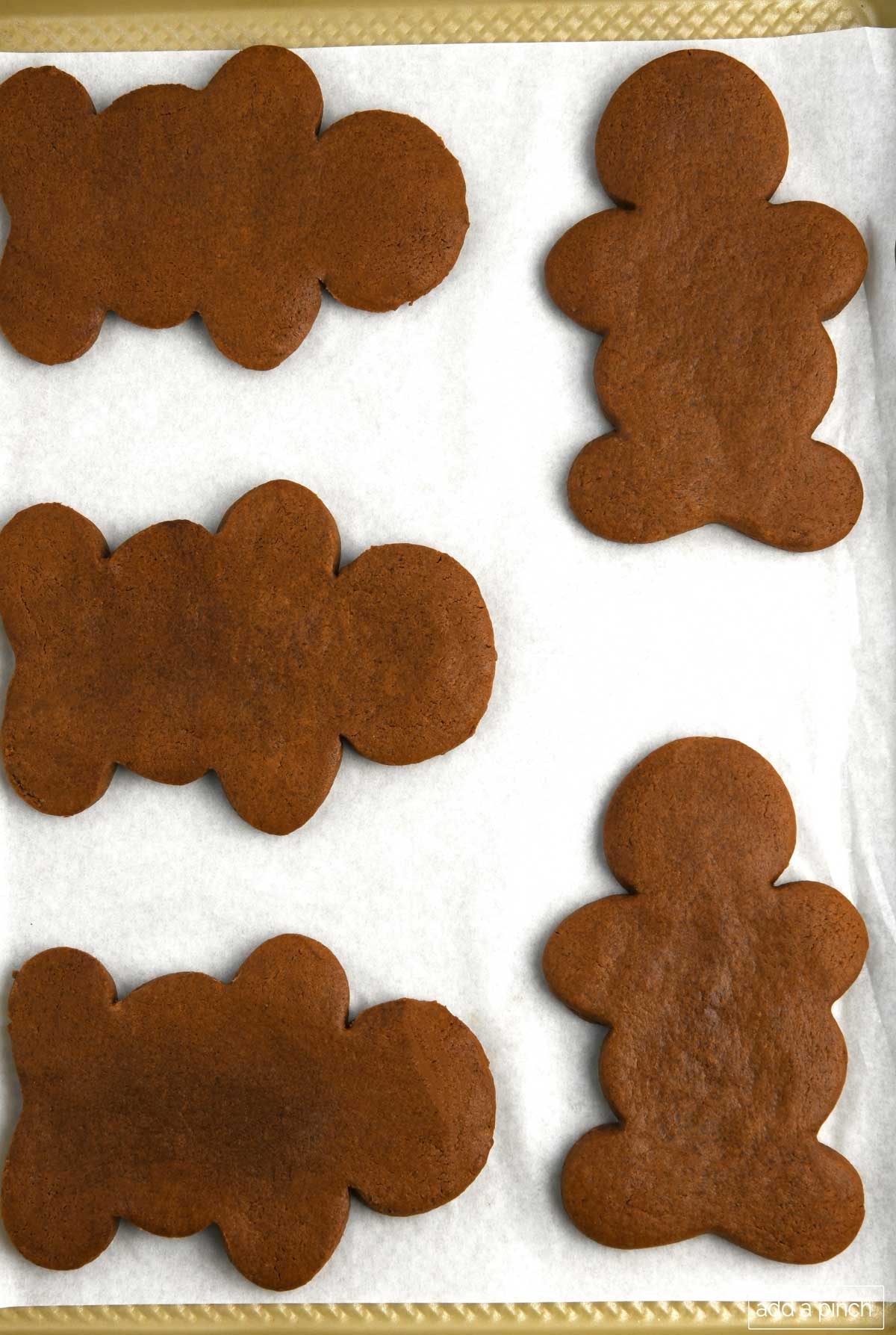 Photo of baked gingerbread men shaped cookies on parchment lined baking sheet.