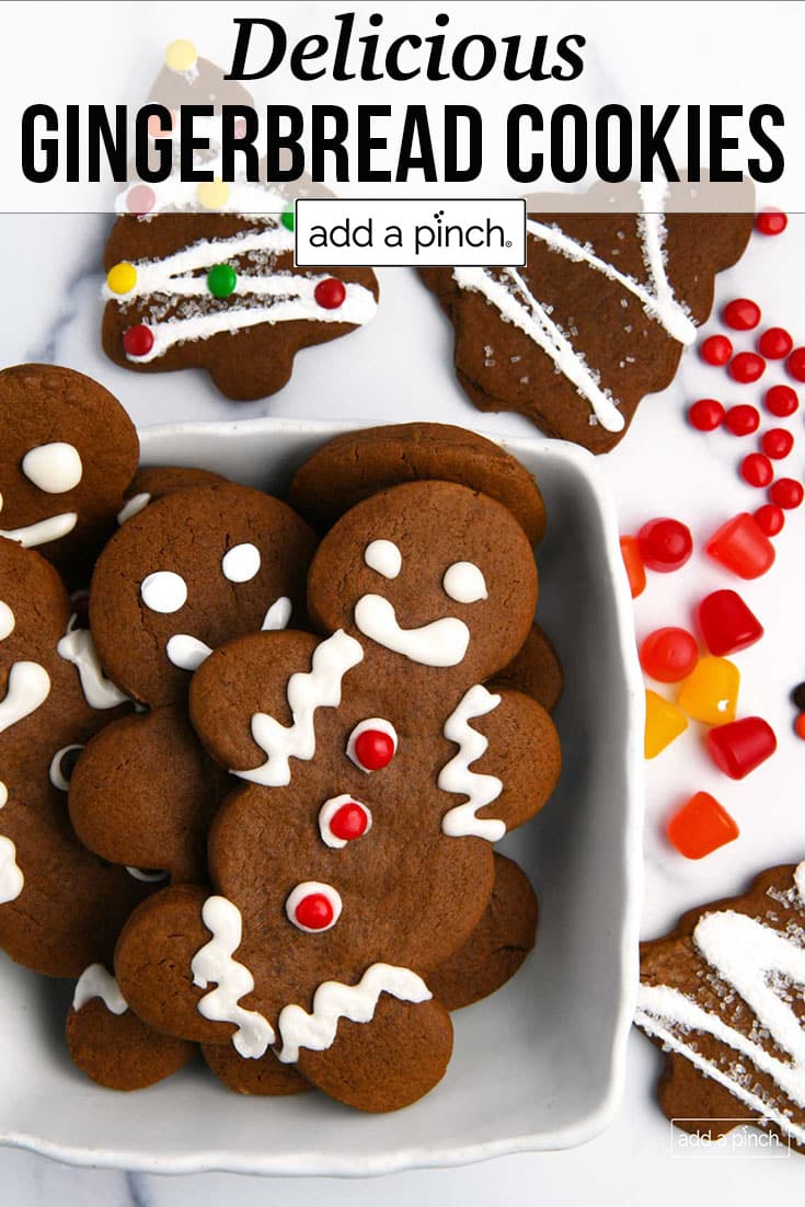 Table of decorated gingerbread trees and gingerbread people, surrounded by candies - with text - addapinch.com
