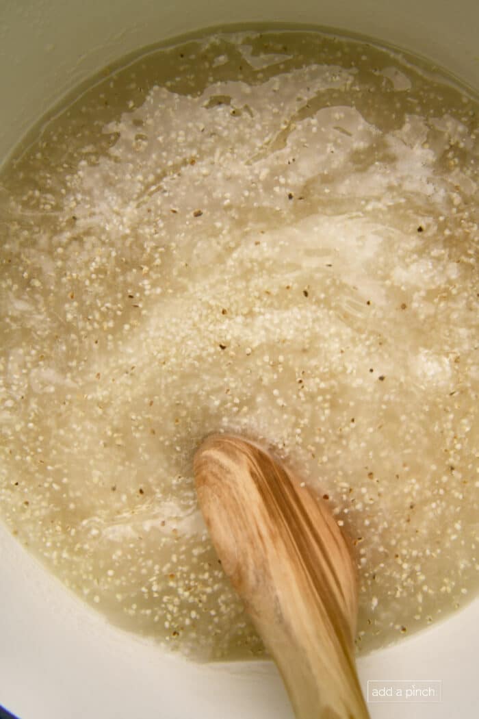 Grits cooking in Dutch oven with a wooden spoon.
