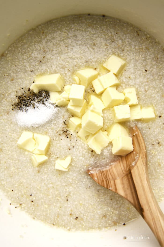 Butter, salt and pepper being stirred into grits.