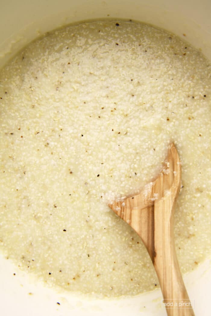 Cooked grits in a Dutch oven with a wooden spoon.