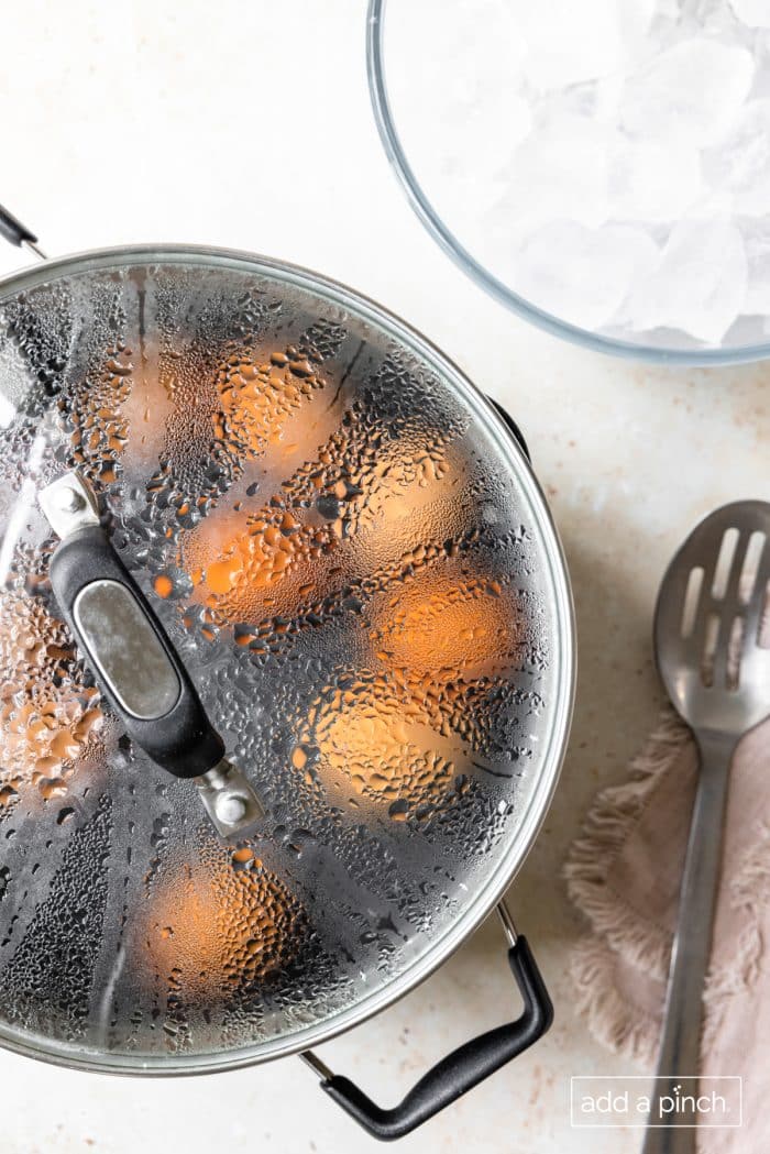 Eggs in pot with lid and slotted spoon.
