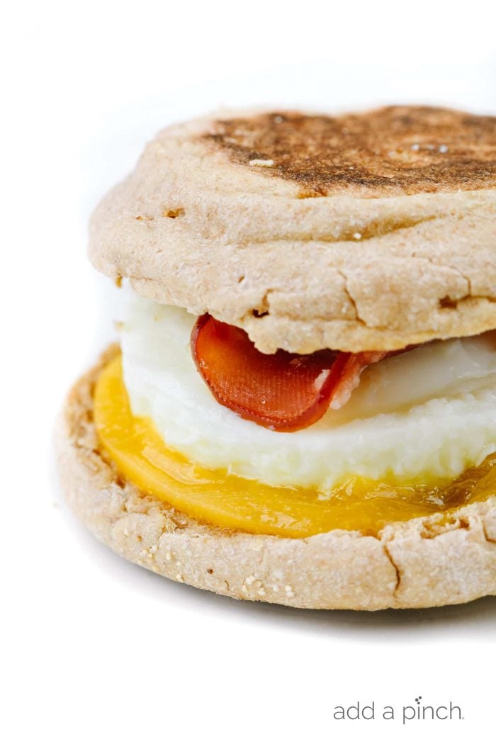 Closeup of side view homemade egg mcmuffin with English muffins filled with cheese, egg, and Canadian bacon on white plate  // addapinch.com