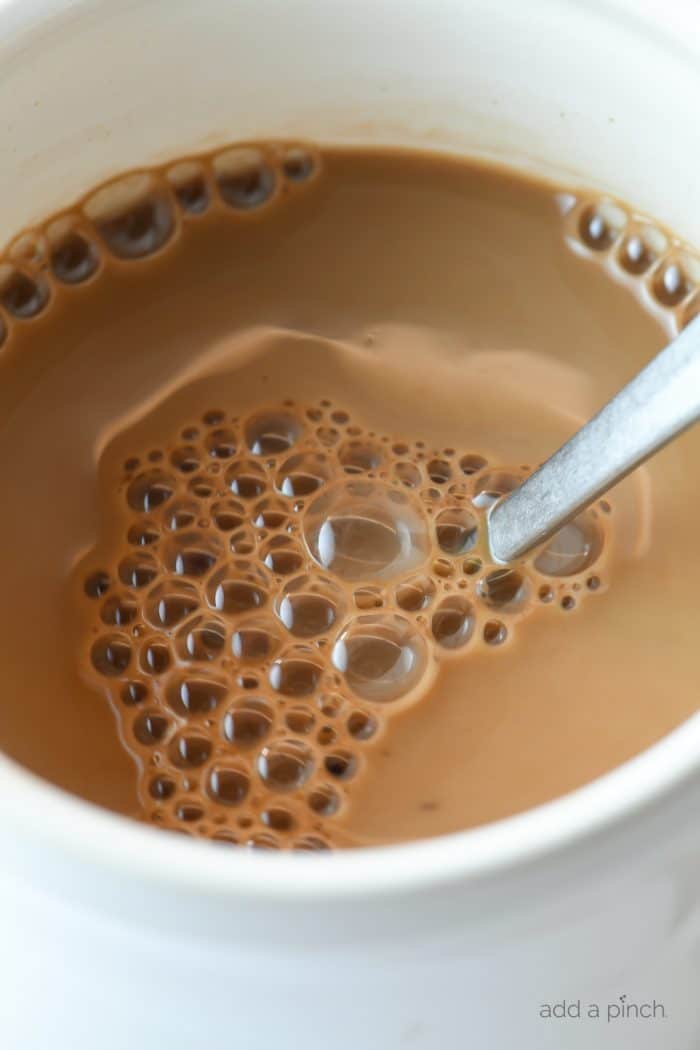 Closeup photograph of hot cocoa in a white mug with a spoon.