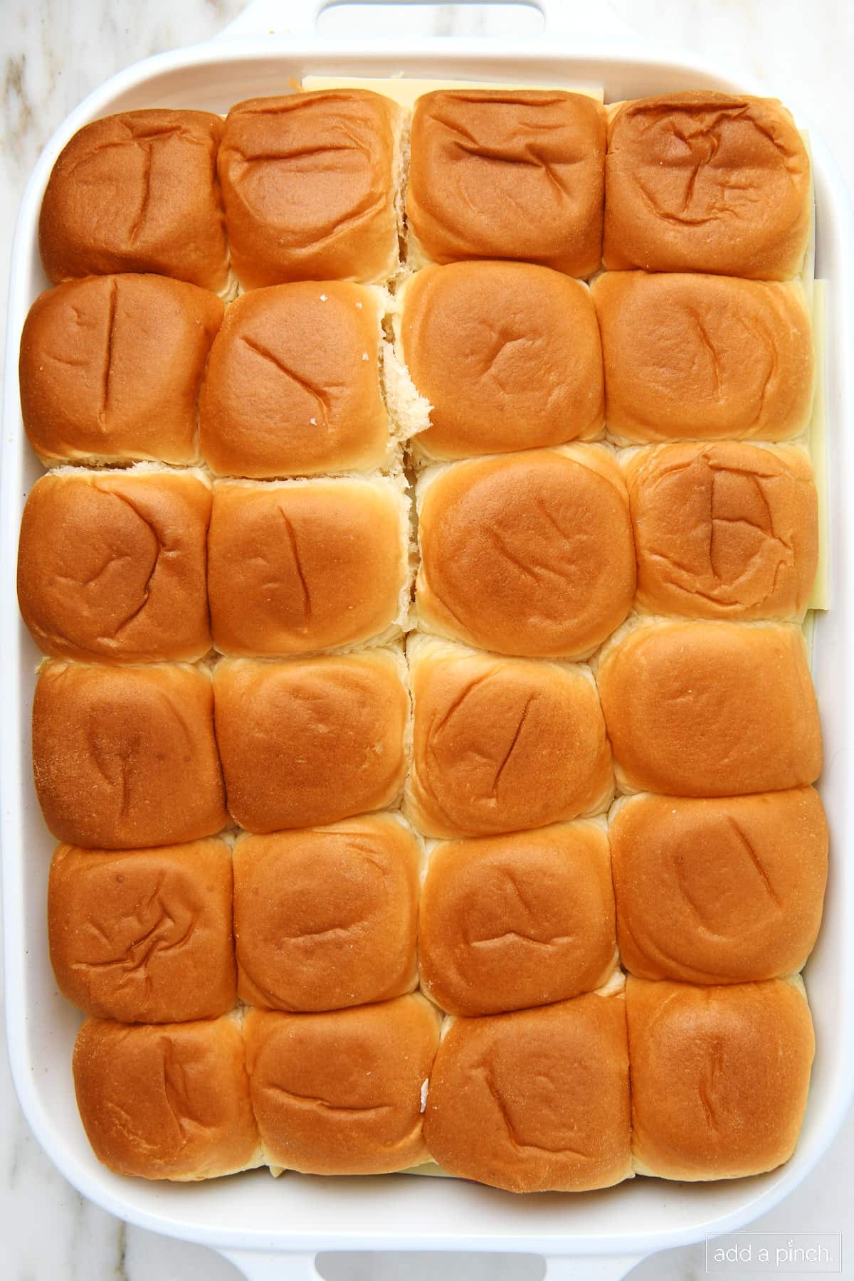 Ham and cheese sliders topped with top half of roll in a 9x13 baking dish.
