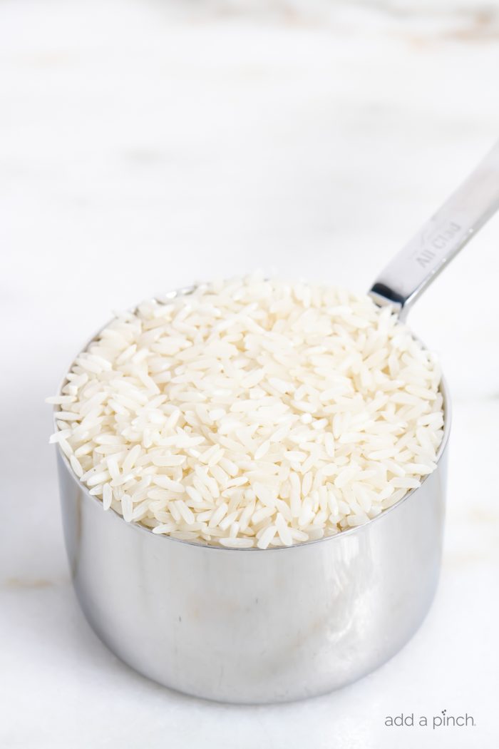 A measuring cup of uncooked white rice on a marble slab. // addapinch.com