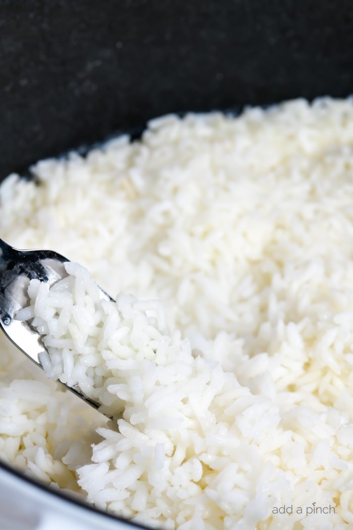 Fluffy white rice with a metal fork in a white Dutch oven. // addapinch.com