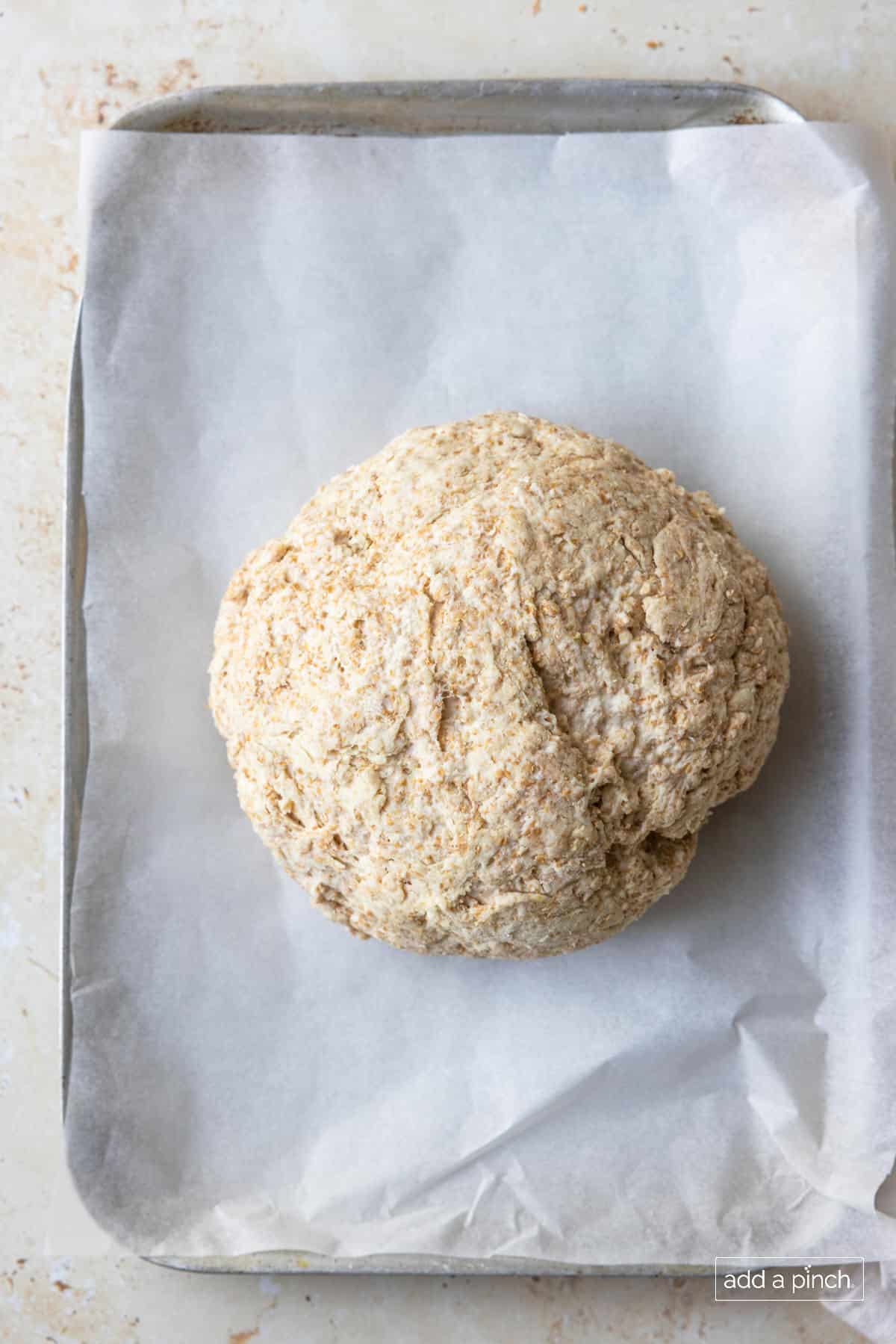 Irish soda bread dough on a parchment lined baking sheet to be baked.