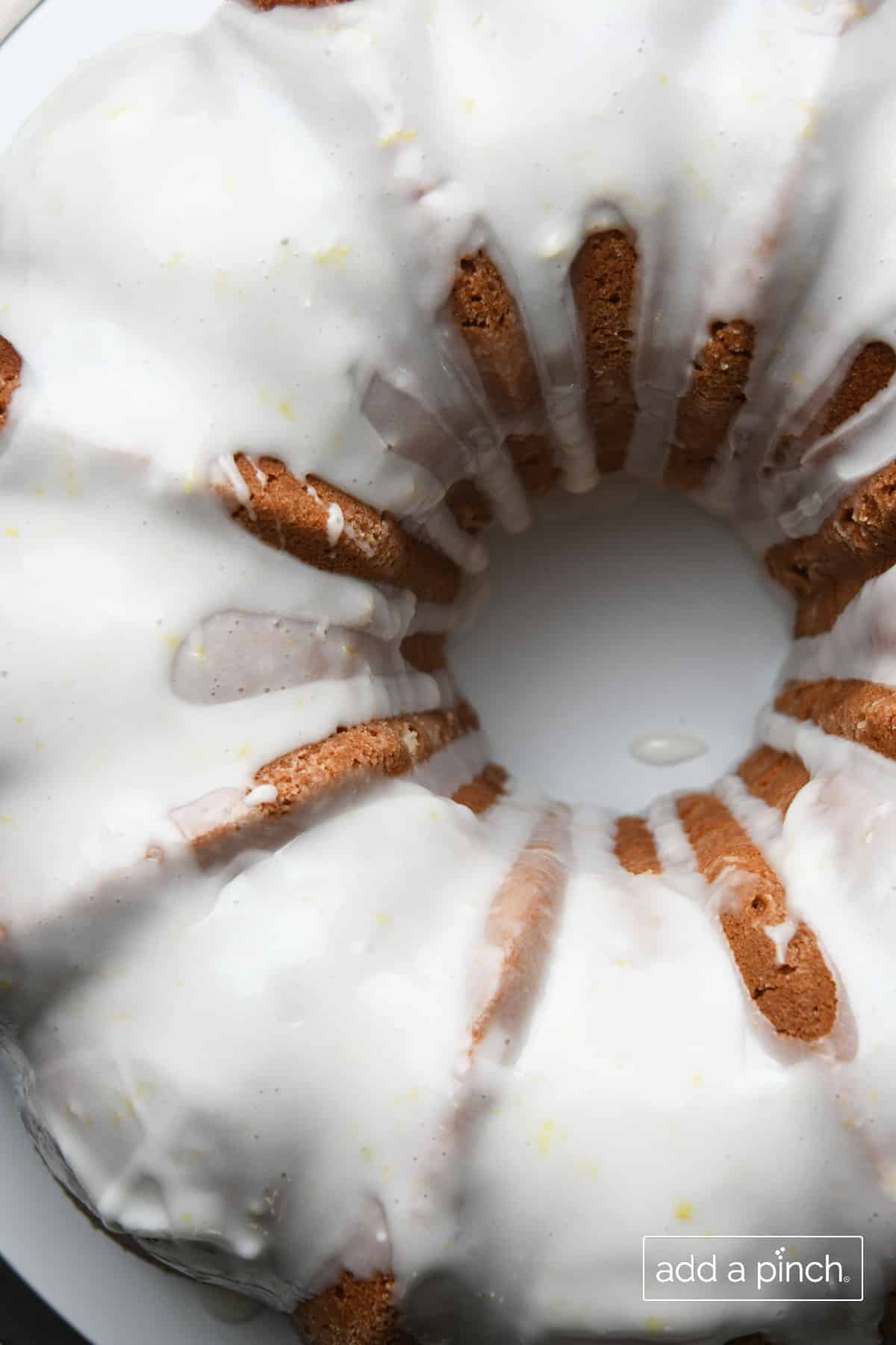 Lemon buttermilk glaze is poured over top of a Lemon Pound Cake on a white dish.