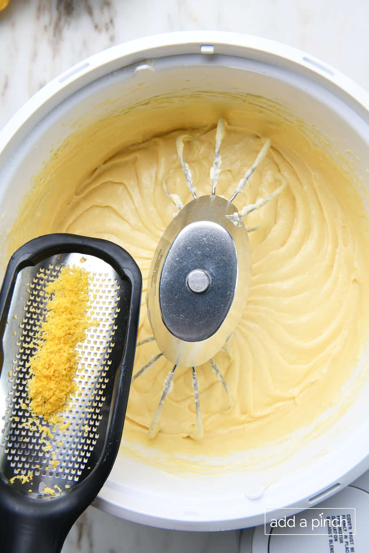 Freshly zested lemon is being added into mixed lemon pound cake ingredients in the stand mixing bowl.