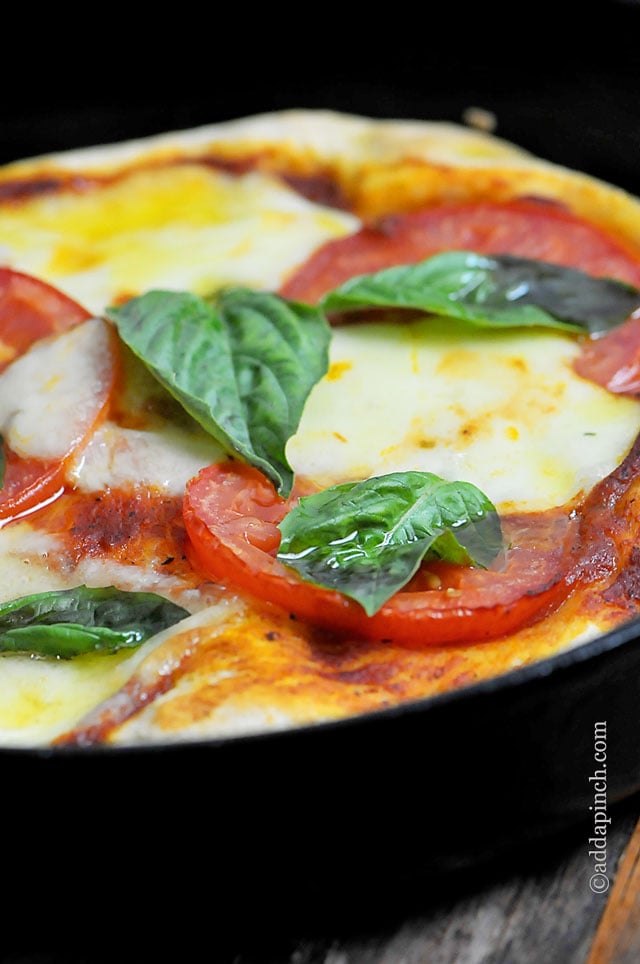 Margherita pizza topped with melted mozzarella, tomato sauce, fresh tomato slices and fresh basil all in a pizza pan.