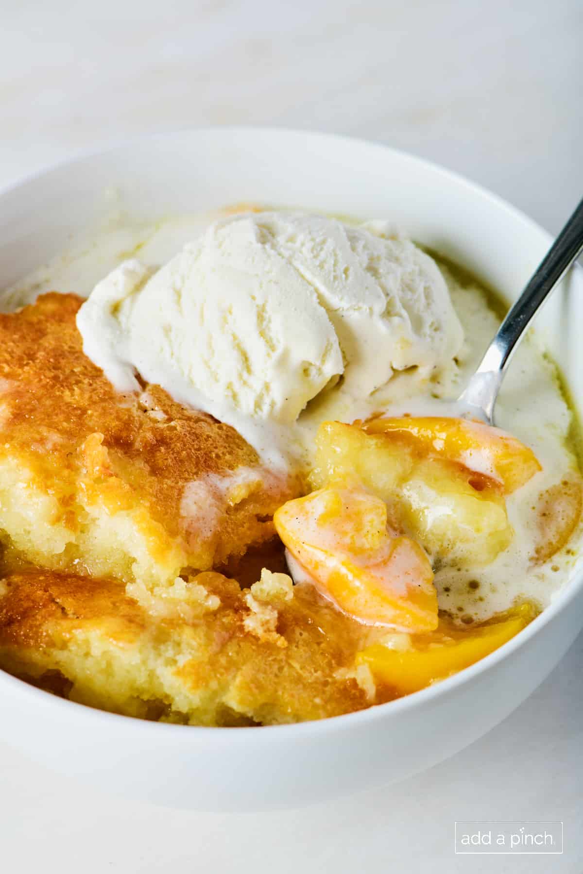 Peach cobbler in a white bowl with vanilla ice cream.