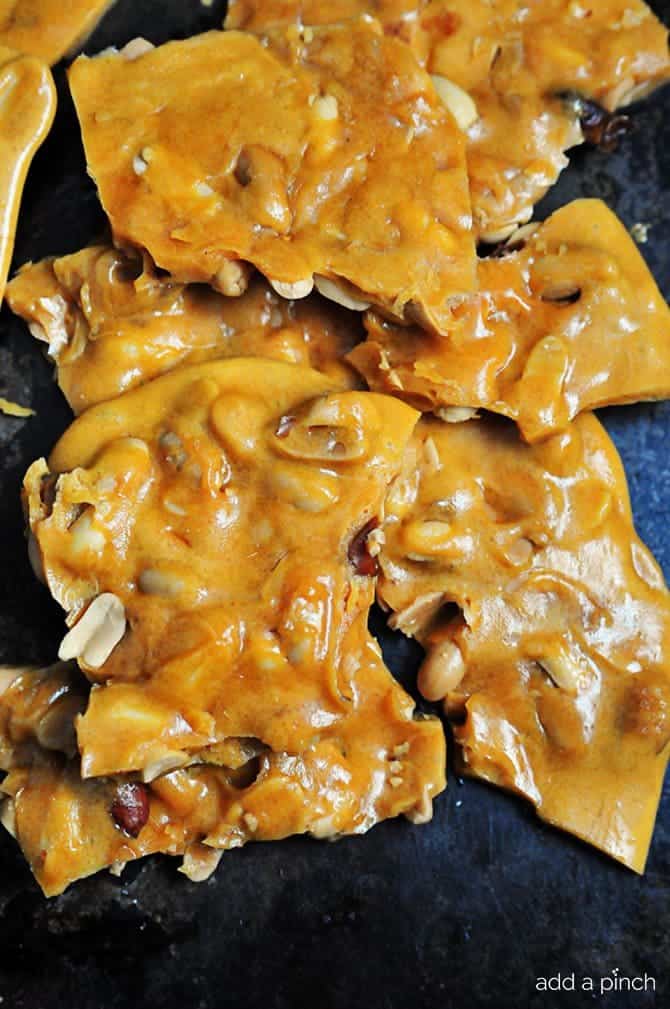 Large broken pieces of peanut filled peanut brittle candy on a dark background.