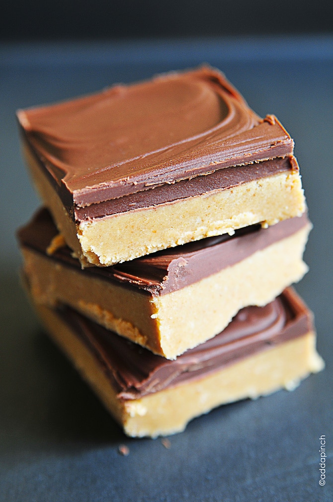 Photo of a stack of three peanut butter bars with a layer of peanut butter filling topped with a layer of chocolate on a dark background.