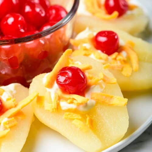 Photo of pear salad on a white plate with a bowl of cherries in the center.
