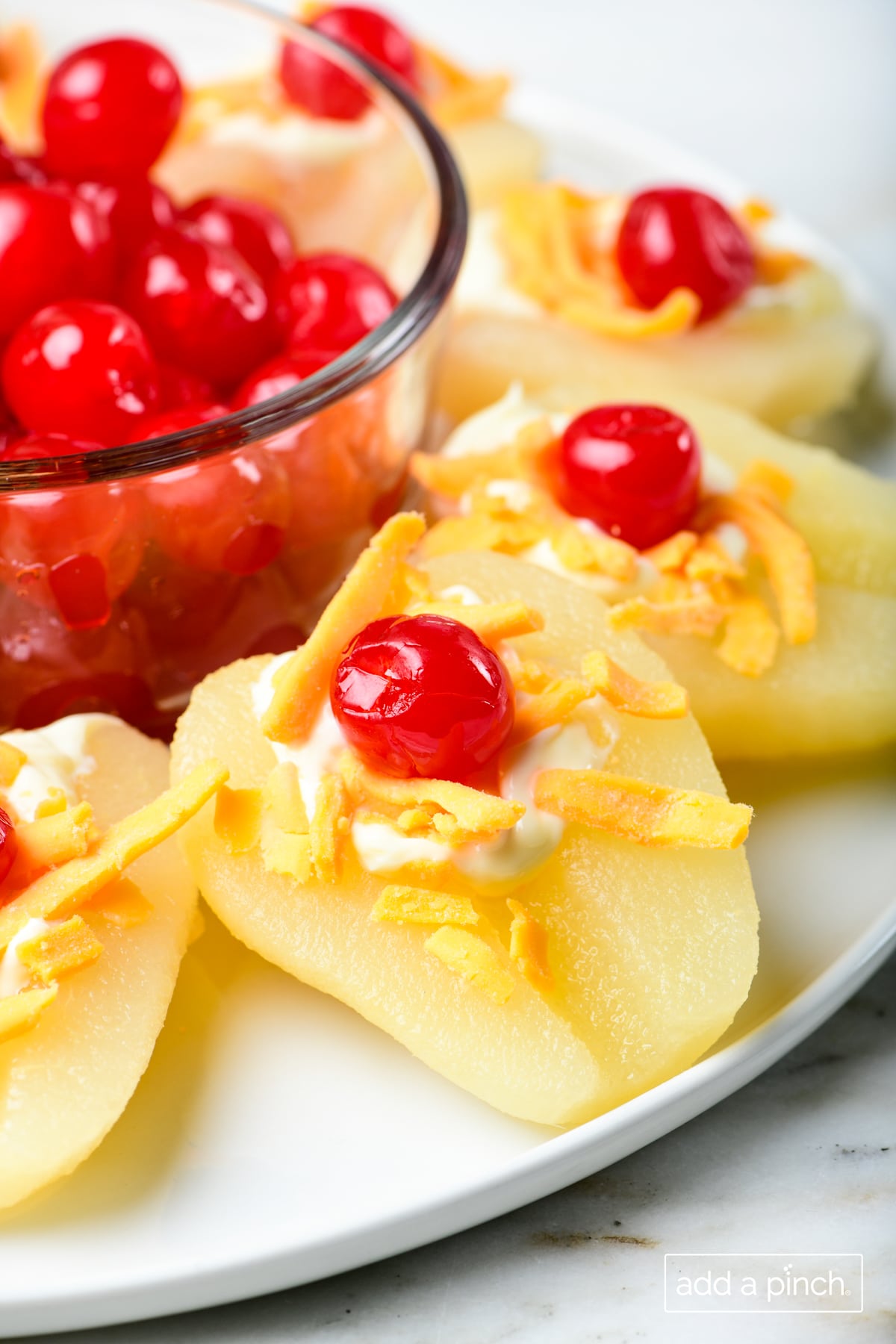 Photo of pear salad on a white plate with a bowl of cherries in the center.