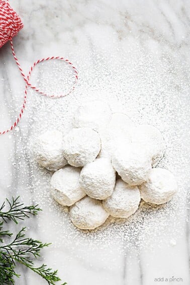 Powdered sugar covered cookies on a marble countertop with greenery and twine.