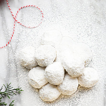 Powdered sugar covered cookies on a marble countertop with greenery and twine.