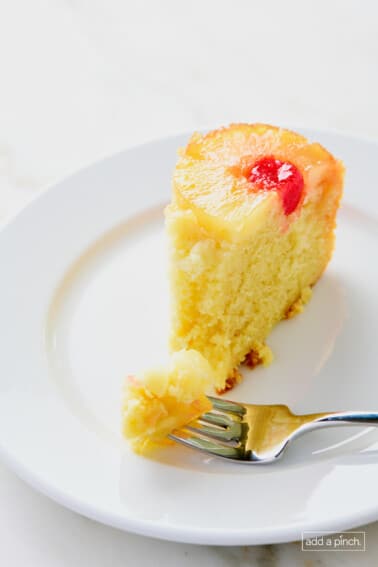 Slice of pineapple upside down cake on a white plate with a fork.