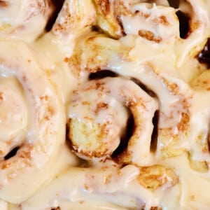 Cream cheese frosting covered cinnamon rolls in a pan.