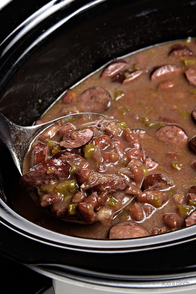 Slow Cooker with cooked red beans recipe with sausage, bell pepper and onions all spooned into a ladle.