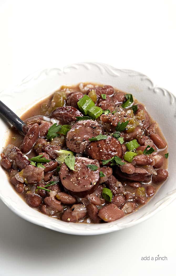 Spoon in a bowl of garnished Red Beans with sausage and bell pepper and onions.