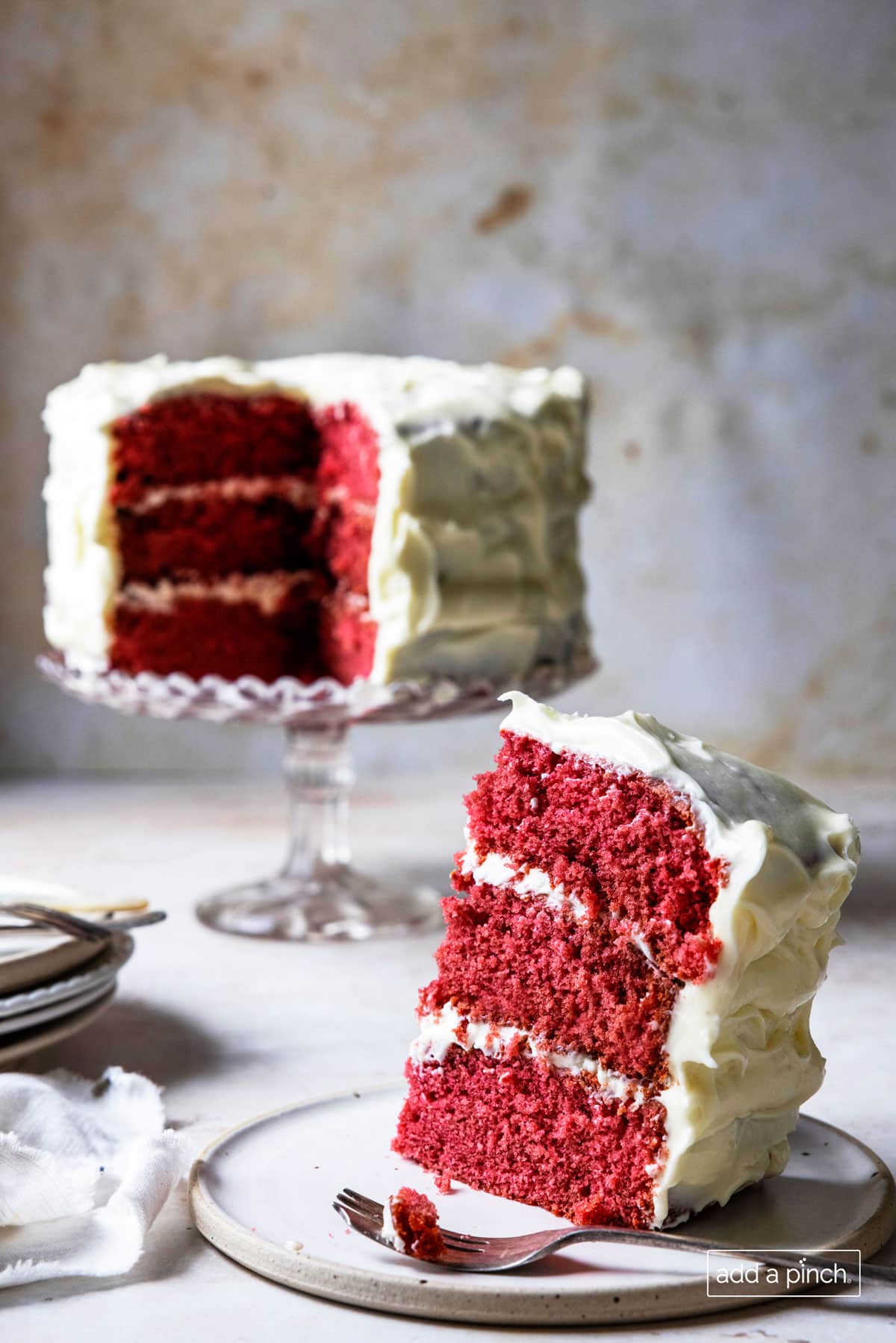 Slice of red velvet cake on a plate with the remaining cake in the background.