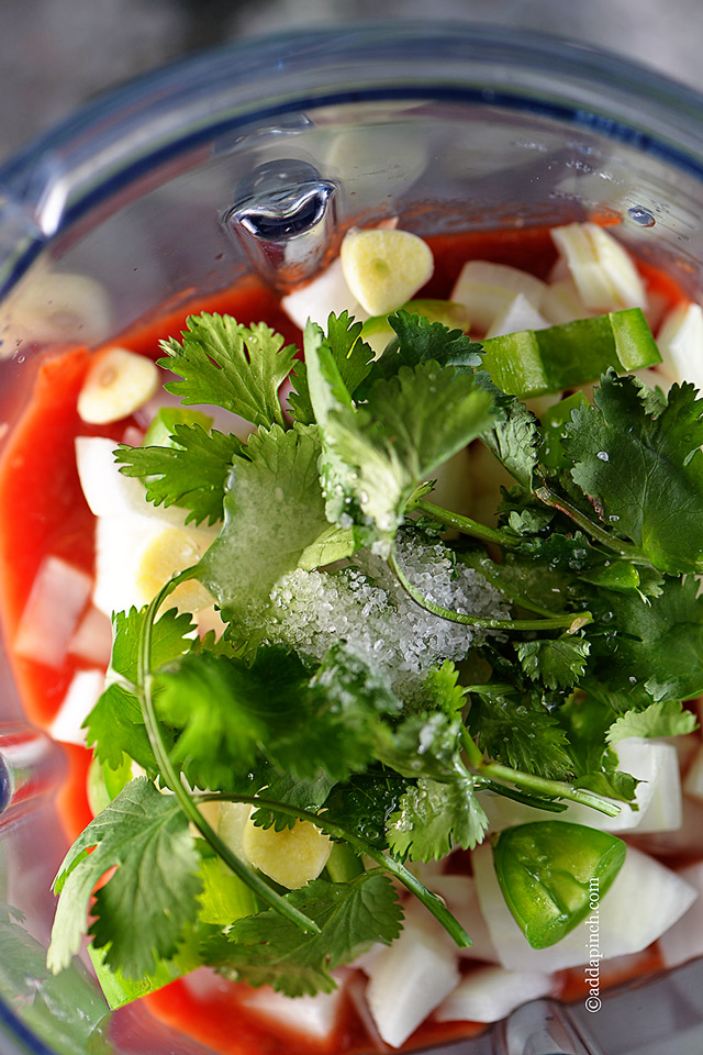 Fresh salsa ingredients of cilantro, tomatoes, garlic, onions and jalapenos in blender jar  - addapinch.com
