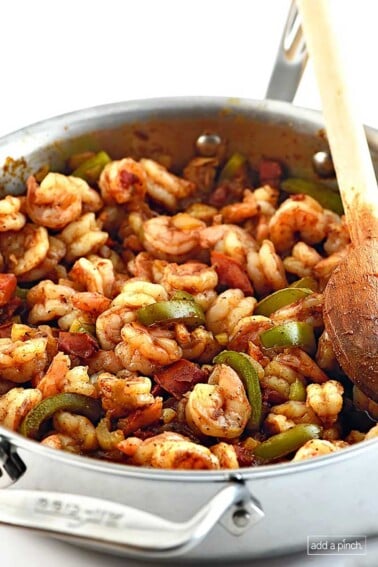 Photo of Shrimp Creole with shrimp, green pepper slices and tomatoes with a wooden spoon in a stainless steel skillet.