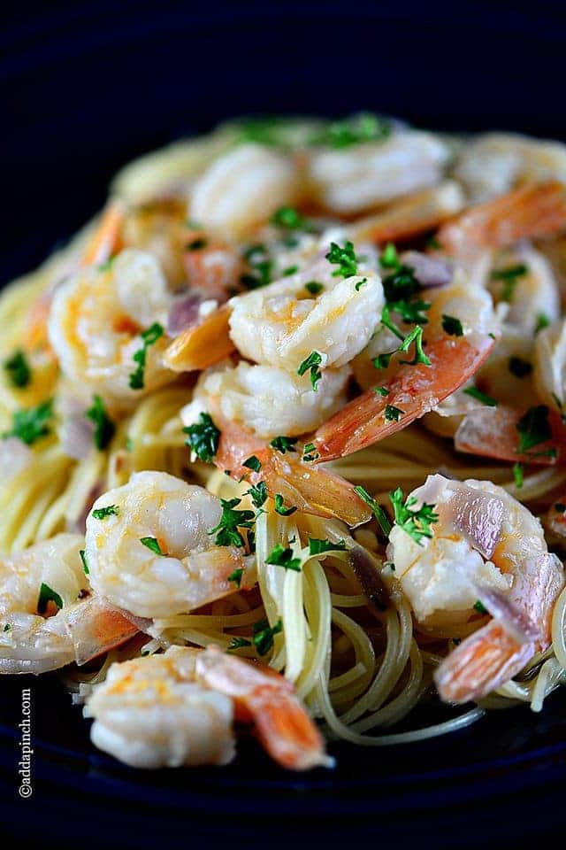 Closeup view of mound of cooked, pink shrimp in scampi recipe, placed on top of pasta and garnished with fresh parsley // addapinch.com