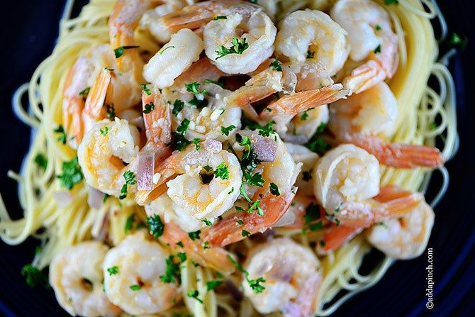 Overhead view of shrimp scampi on pasta, showing shrimp, garlic, red onion and fresh parsley // addapinch.com