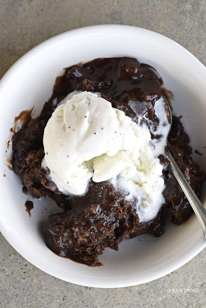 Bowl of chocolate cobbler and a spoon topped with vanilla ice cream.