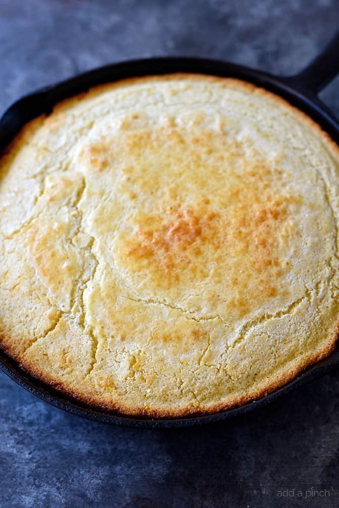 Golden brown cornbread with crisp edges in a cast iron skillet on a black granite counter.