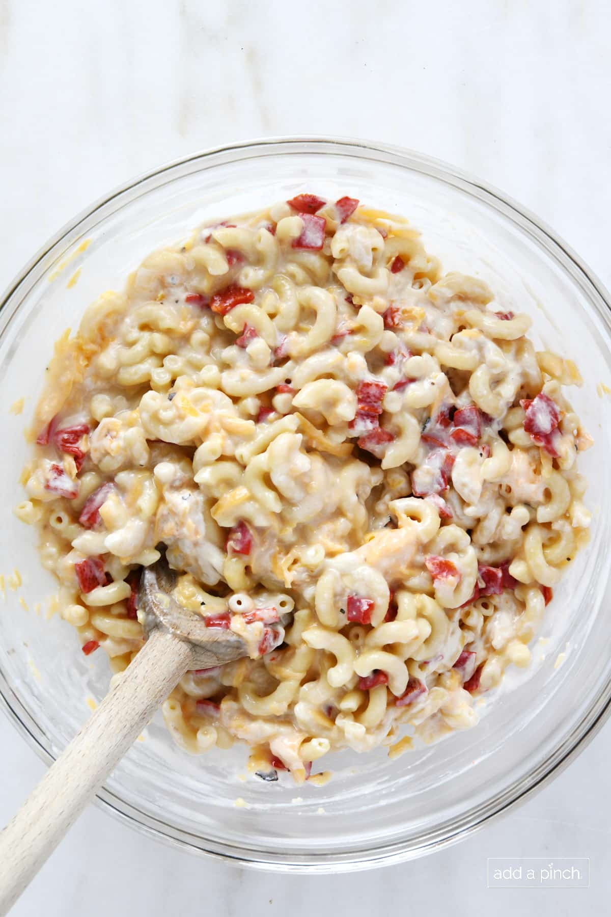 Glass bowl with noodles, pimentos, soup, mayo and cheese mixed well with a wooden spoon.