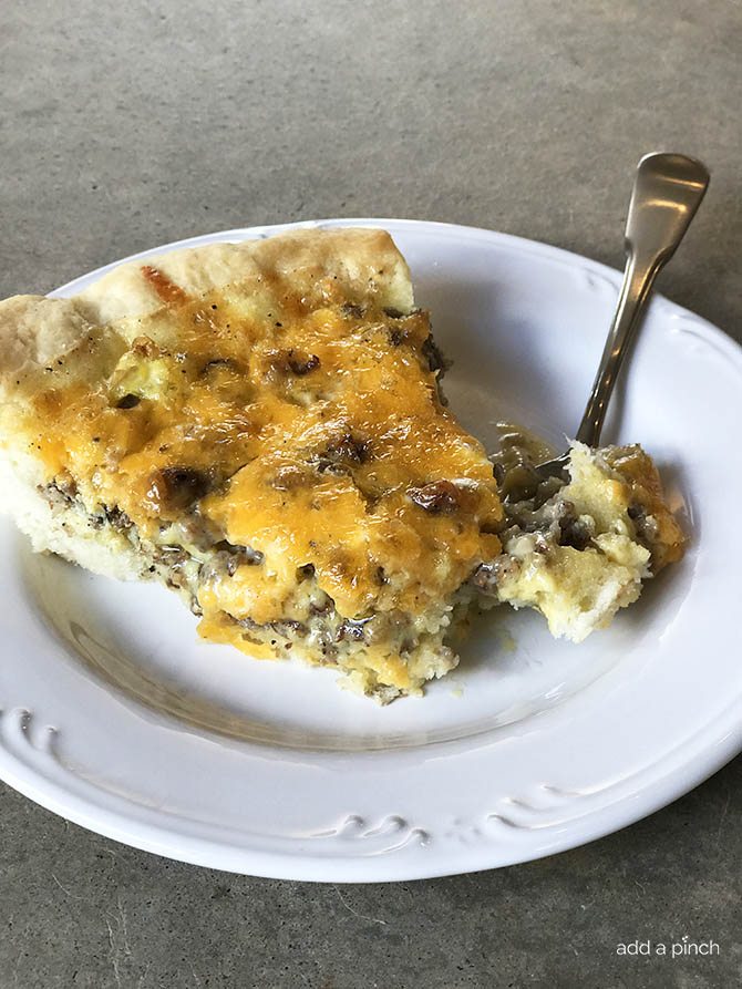 Photo of sausage cheddar quiche with pastry crust and fork with bite of quiche on white plate.