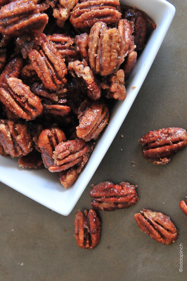 Easy cinnamon pecans in a white serving bowl on a concrete surface.